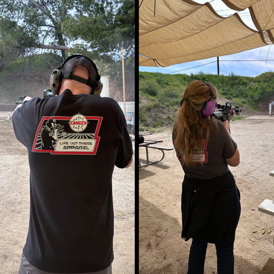 Life Out There Apparel “Kill Cancer” Black Unisex tee shirt has picture of a man shooting a sign that says cancer on it & the bullet rounds coming out of the gun have  “chemo” written on them. This is a man and women showing the back of the tee shirt while shooting at a gun range 