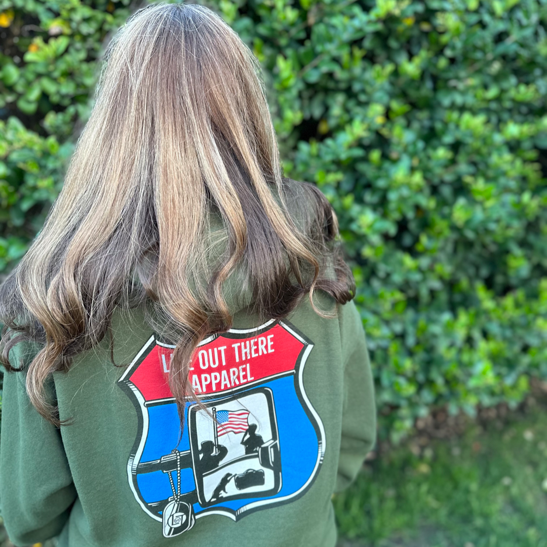 Life Out There Apparel “Leave It Behind” - Military Green Unisex Pullover hoodie has a truck side mirror with the reflection of a male, female & K9 soldiers saluting the American flag - bringing awareness to P. T. S. D. (post traumatic stress disorder). This is a photo,of a woman wearing the hoodie showing the back design.