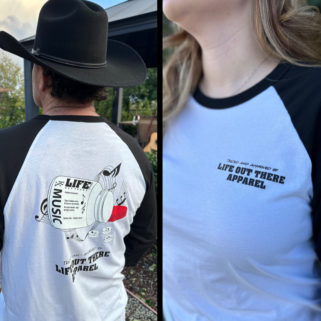 Black & White Life Out There Apparel “Music Is Medicine “ Unisex Raglan 3/4 tee shirt is a medicine pill bottle tipped over with pills that have fallen out, that have music notes on them. This photo has a man in a cowboy hat showing the back of the shirt & a women showing the front of the shirt.