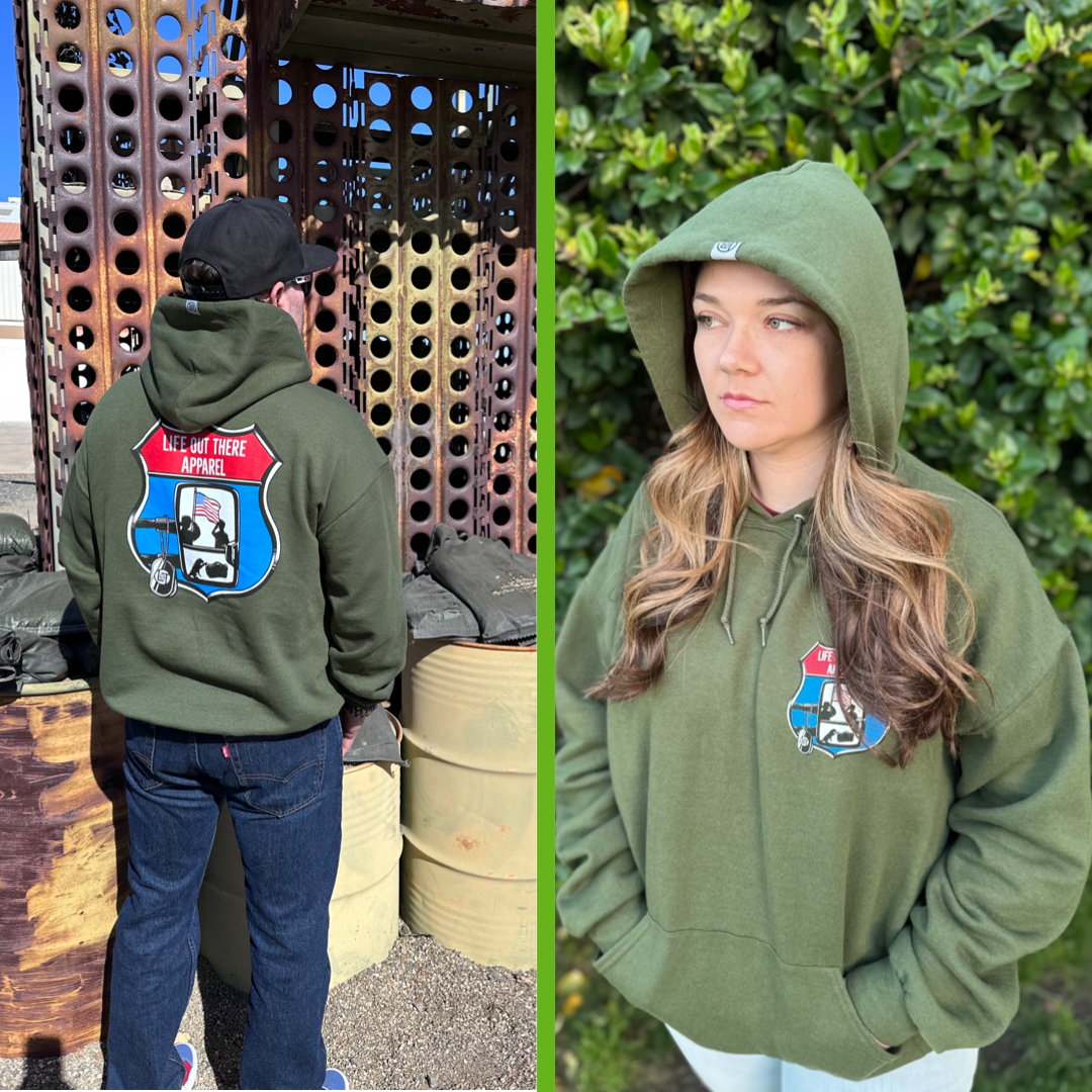 Military Green Unisex Pullover hoodie from Life Out There Apparel “Leave It Behind” the design has a truck side mirror with the reflection of a male, female & K9 soldiers saluting the American flag - bringing awareness to P. T. S. D. (post traumatic stress disorder). This is a photo,of a man wearing the hoodie showing the back design, standing next to a bunker & a women showing the front design.
