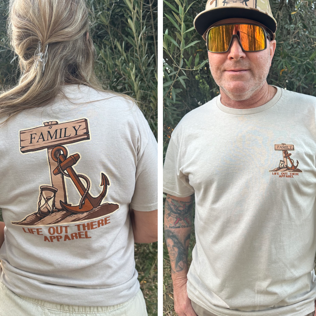 Outdoors, a person in sunglasses models a Sandstone Unisex Time Flies T Shirt by Life Out There Apparel. The front boasts a small logo, and the back is adorned with an anchor and compass design alongside the words "Time Flies" and "Family." Tattoos on one arm enhance the casual look.