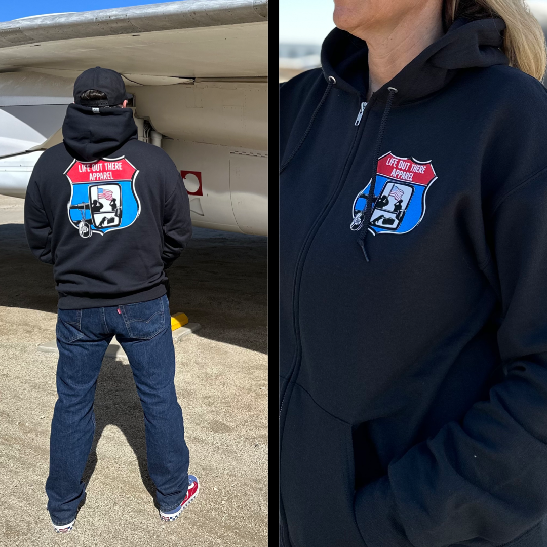 Black “Zip Up” Unisex hoodie from Life Out There Apparel - “Leave It Behind” has a truck side mirror with the reflection of a male, female & K9 soldiers saluting the American flag - bringing awareness to P. T. S. D. (post traumatic stress disorder). There’s a man wearing the hoodie showing the back standing next to a fighter jet & a women wearing the hoodie showing the front.