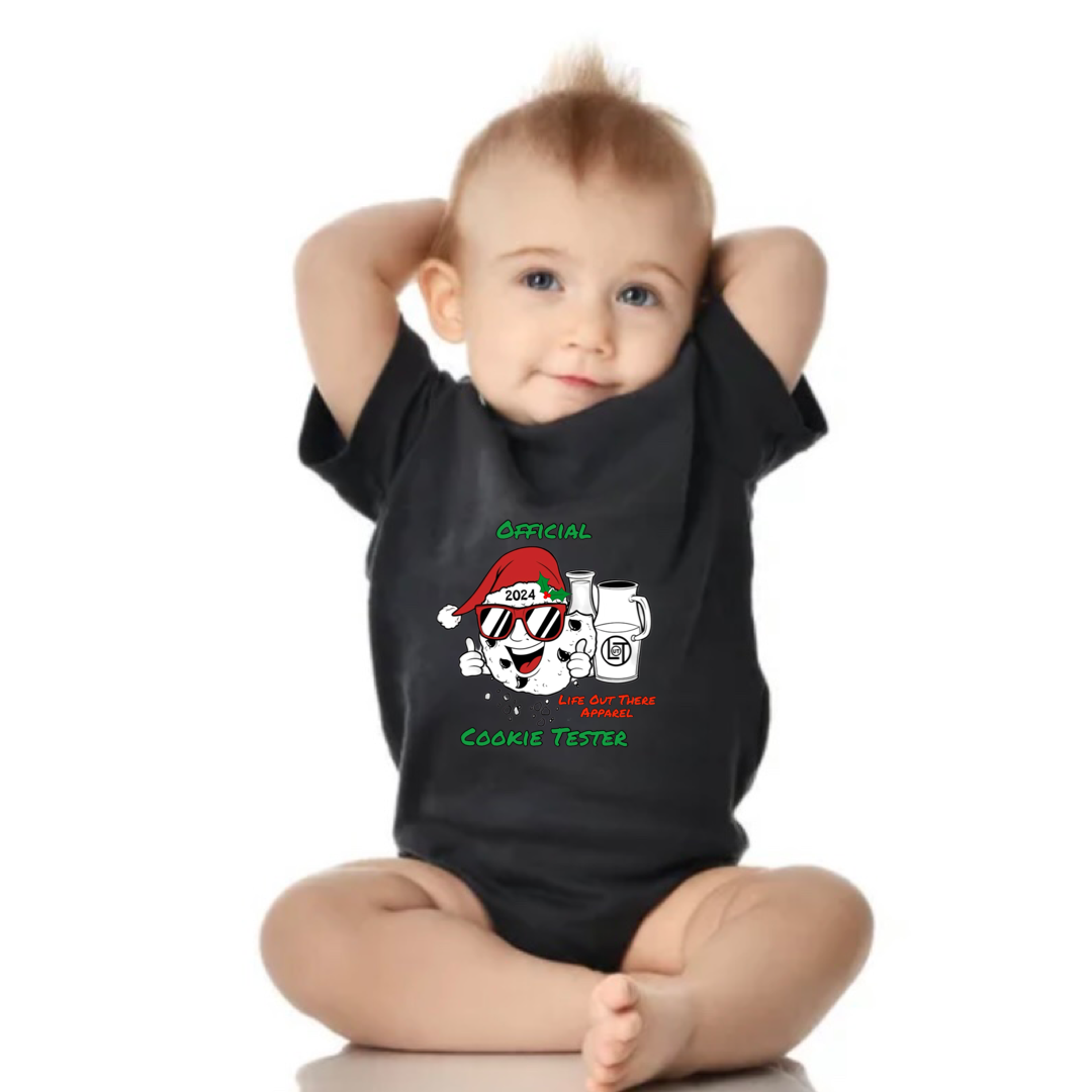 Black short sleeve baby shirt with a cartoon cookie wearing a Santa hat and sunglasses labeled "2024," alongside glass milk cartons. Text reads, "Life Out The Apparel / official cookie tester”.