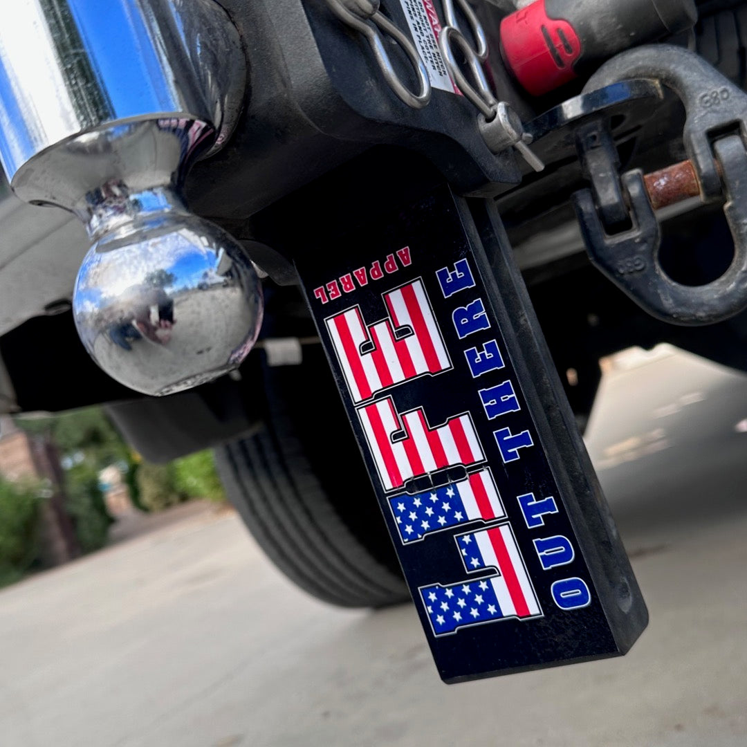 Close-up of a vehicle's hitch showcasing the Life Out There - Freedom Sticker from Life Out There Apparel, featuring the text "USA OUT THERE" in patriotic red, white, and blue with stars and stripes. The setting is a sunny outdoor area with blurred greenery and pavement in the background.