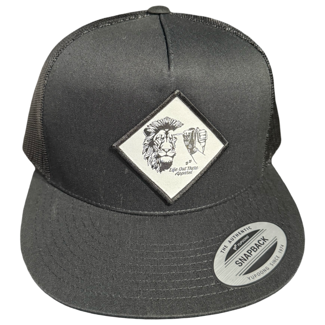 The Not All There - Flat Bill SnapBack Trucker Hat in black by Life Out There Apparel features a front patch with a lion’s face, raised fist, Live Out Truth Apparel, and NOT ALL THERE, plus a silver The Authentic Yupoong Snapback sticker on the brim.