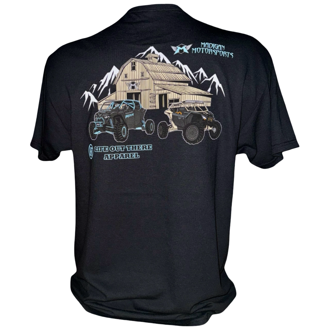The Unisex - Side X Side Tee - Black by Life Out There Apparel features two Side X Side vehicles before a barn and mountains, with "Madigan Motorsports" and "Life Out There Apparel" text—ideal for off-road fans.