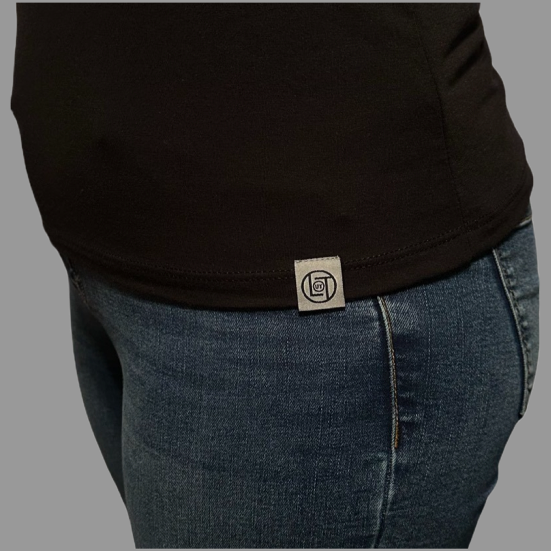 Close-up of a person wearing the Thanks Dad Women's T Shirt in black by Life Out There Apparel, paired with blue jeans. The shirt features a small circular tag with the brand's logo on the side hem, highlighting life's little details we often overlook. The background is a plain gray color.