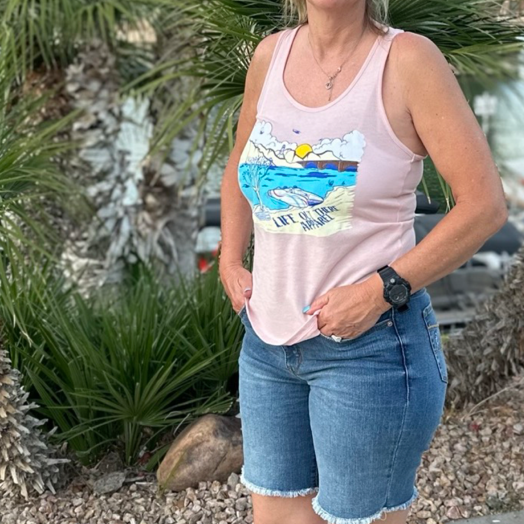 Dressed in the Vintage Pink "Havasu Women's Tank Top" from Life Out There Apparel, paired with denim shorts, an individual effortlessly captures the essence of summer by standing amidst palm trees. With hands tucked into their pockets and a watch on their wrist, they radiate the laid-back spirit reminiscent of Lake Havasu.