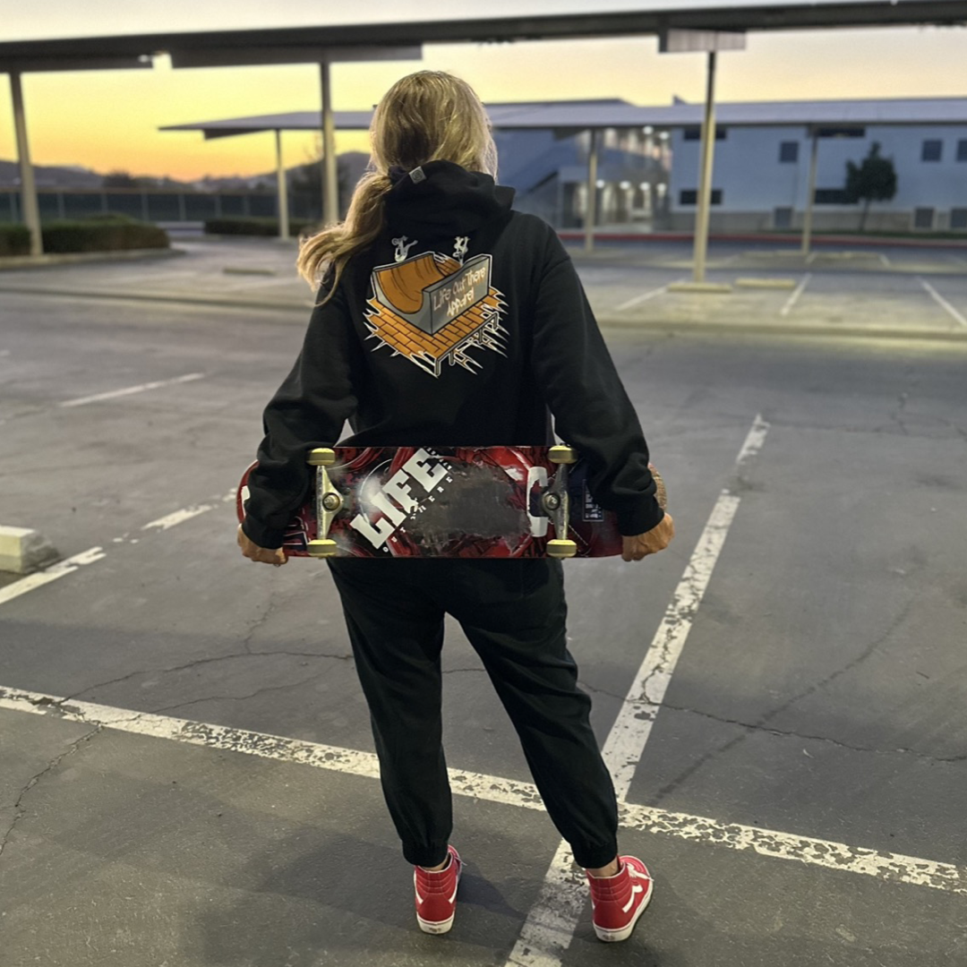 Life Out There Apparel “Fun is Not a Crime” Black Unisex hoodie has a skateboarder and bmx rider having fun on a half pipe skateboard ramp. A women showing the back of the hoodie holding a skateboard.