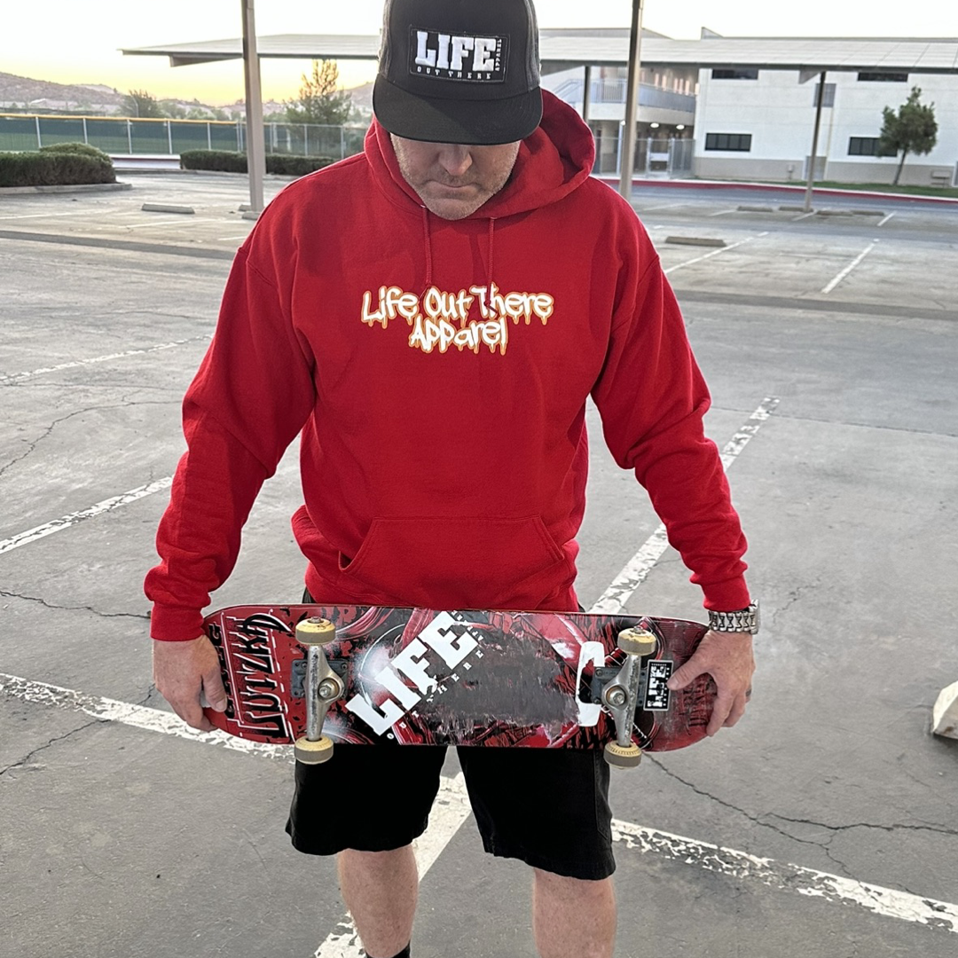 Life Out There Apparel “Fun is Not a Crime” Red Unisex hoodie has a skateboarder and bmx rider having fun on a half pipe skateboard ramp. A man showing the front of the hoodie, holding a skateboard. The front design looks like it’s spray painted.