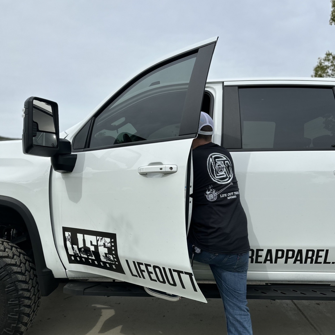 Life Out There Apparel “Branded” Unisex black tee shirt is a round logo of the companies initials, made with a hot branding iron. This is a photo of a man wearing the shirt getting into his truck.
