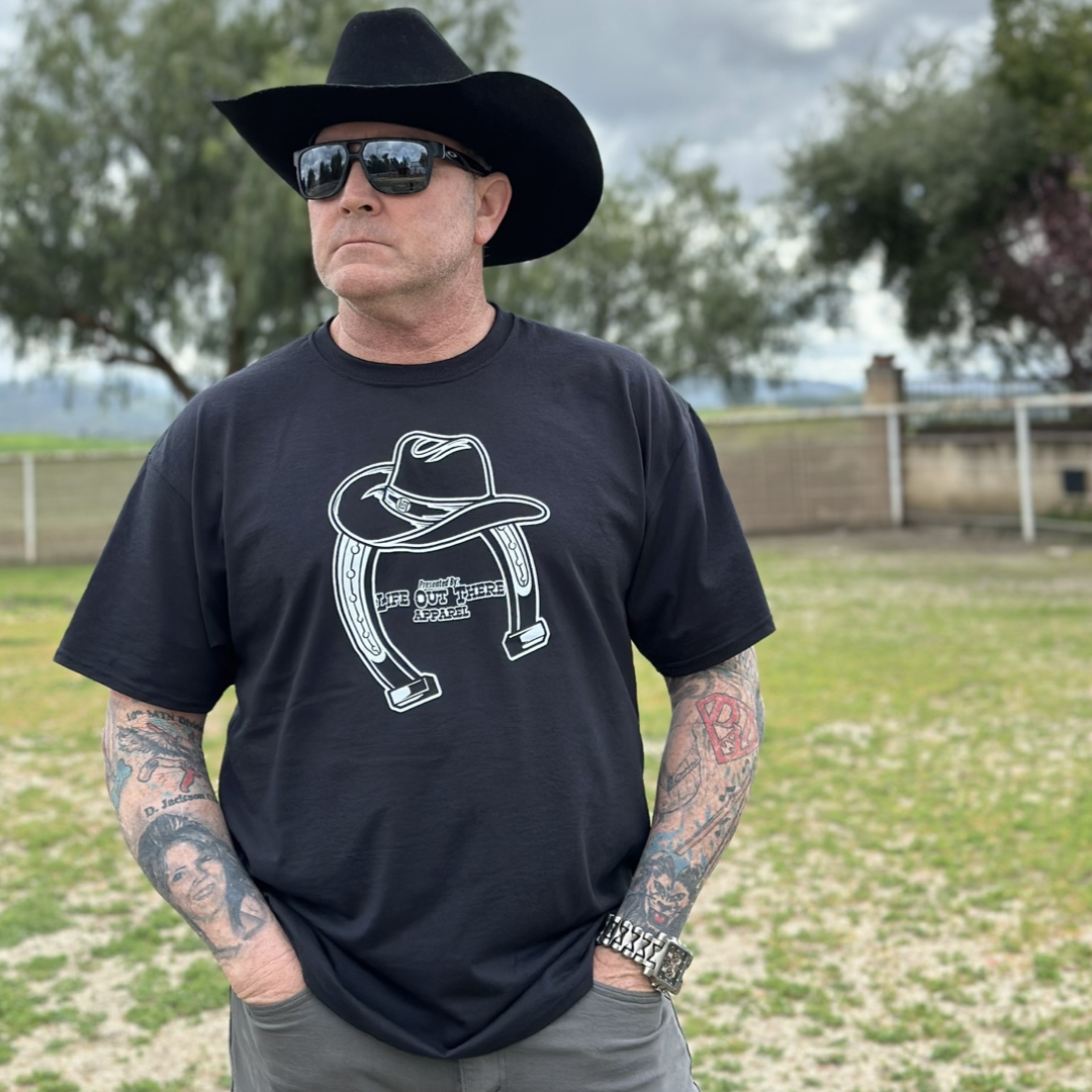 “ONWARD & UPWARD” Tour :
Life Out There Apparel “ONWARD & UPWARD” Tour Black Unisex tee is a country concert design with a cowboy hat & horseshoe on the front and back, with all the design names from the past 2 years (instead of city & tours dates) this photo is of a man wearing a cowboy hat standing on a ranch.