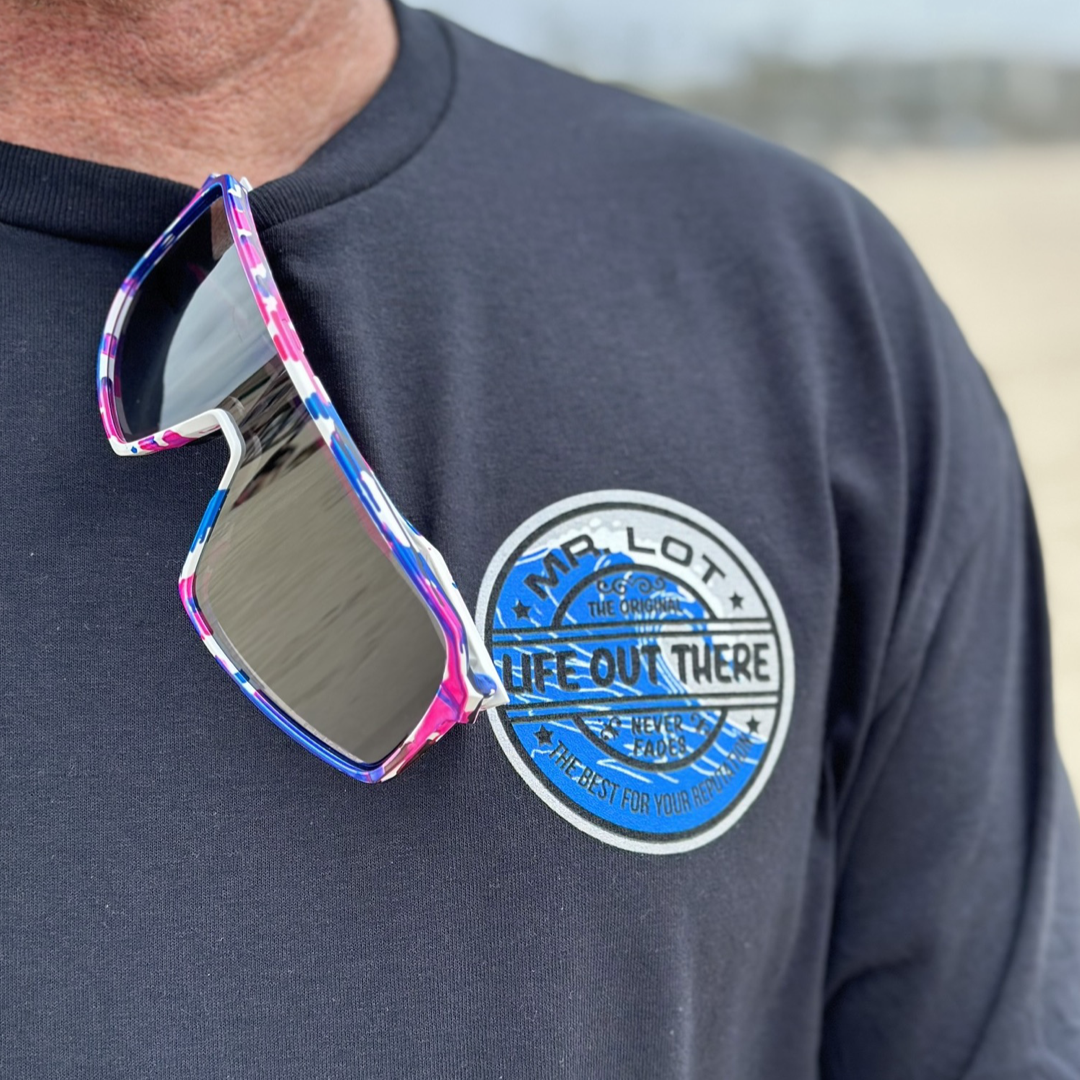 Wearing a Unisex Summer Vibes T-Shirt in black from Life Out There Apparel, a person radiates SUMMER VIBES. Vibrant and oversized sunglasses are clipped to the shirt, evoking memories of leisurely days with MR. ZOGS SEX WAX and surf escapades. The blurred background encapsulates the feeling of freedom.
