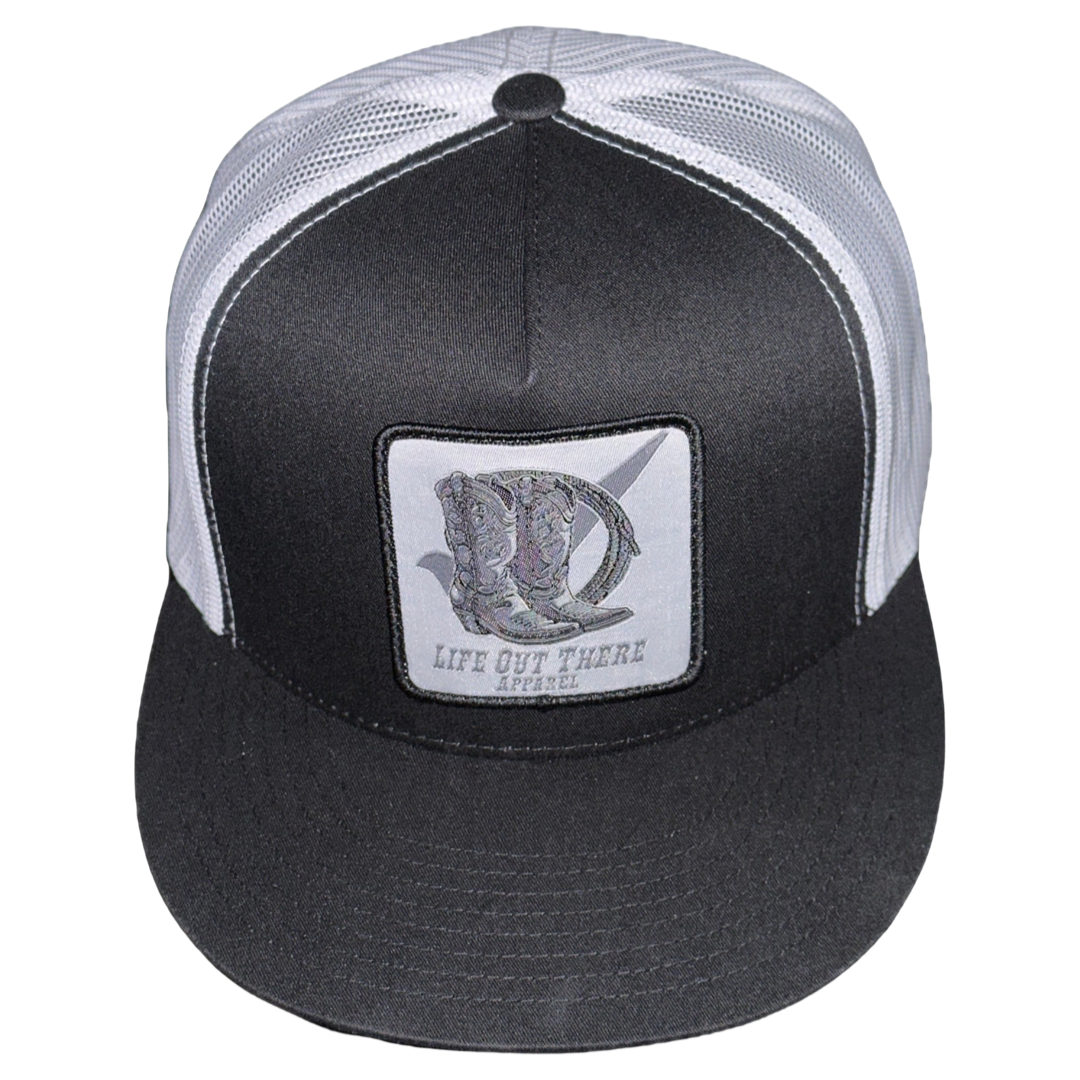 This BOOT CHECK Flat Bill SnapBack Trucker Hat in Black/White from Life Out There Apparel features a mesh back and an embroidered patch on the front panel showcasing a fish design and the brand's text. It also comes with a flat black brim.