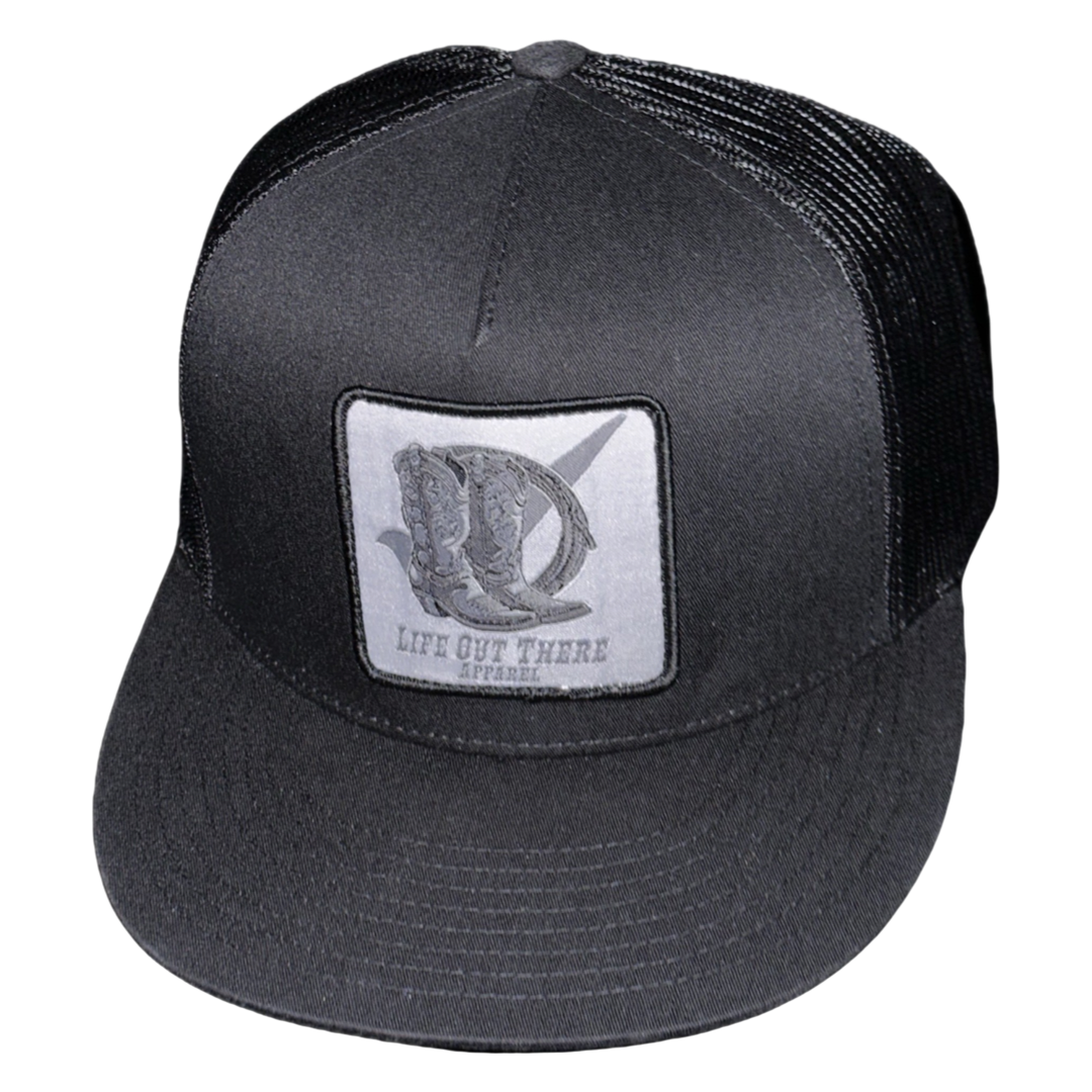 The BOOT CHECK - Flat Bill Snapback Trucker Hat in black from Life Out There Apparel features a front patch with a stylized letter D and the brand name.