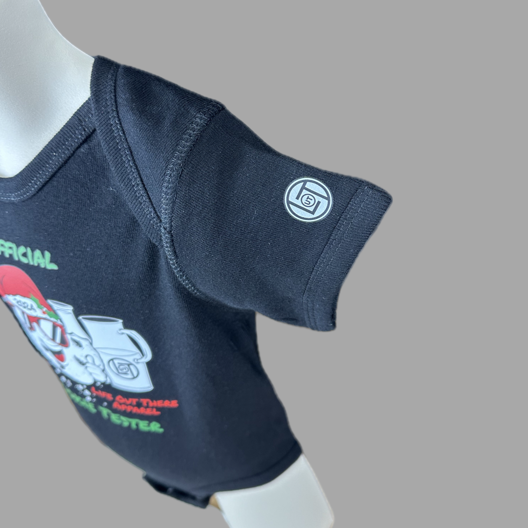 Black short sleeve baby shirt with a cartoon cookie wearing a Santa hat and sunglasses labeled "2024," alongside glass milk cartons. Text reads, "Life Out The Apparel / official cookie tester”.