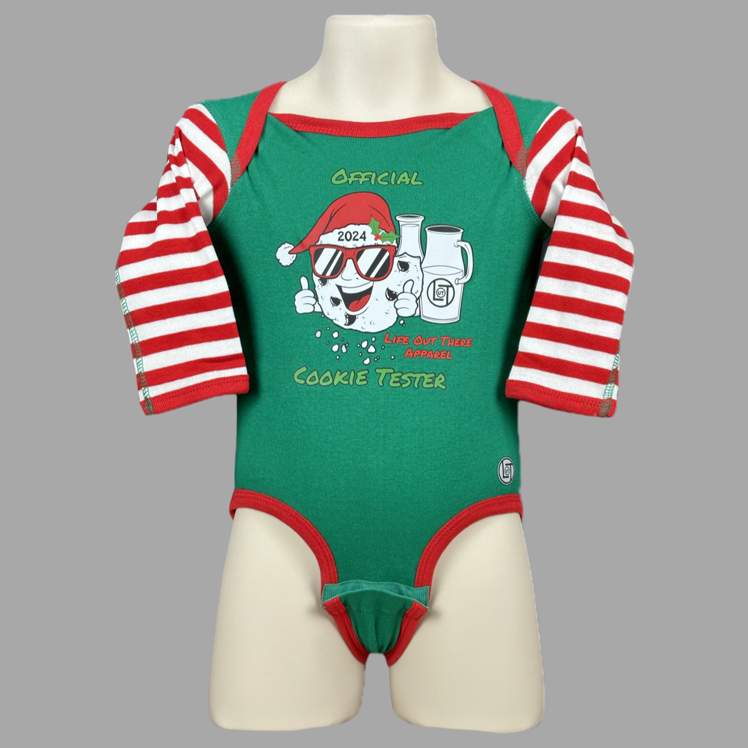 Green long sleeve baby shirt with red & white striped sleeves with a cartoon cookie wearing a Santa hat and sunglasses labeled "2024," alongside glass milk cartons. Text reads, "Life Out The Apparel / official cookie tester”.
