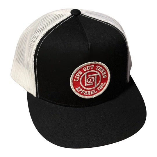 A stylish black and white snapback trucker hat with a mesh back, featuring a red and white circular patch that proudly displays the text Life Out There Apparel.