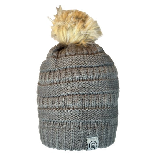 Introducing the Women's Pom Beanie 2.0 - Charcoal by Life Out There Apparel, featuring a stylish knitted design in charcoal grey with horizontal ribbed patterns. Topped with a fluffy beige pom-pom, this women's beanie is accented with a small logo patch on the rim, set against a plain white background.