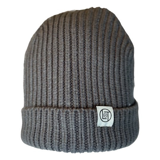 The Men's Knit Beanie - Charcoal from Life Out There Apparel features a charcoal grey ribbed knit design with a folded brim and a sewn tag showcasing a simple, circular logo on the front. It is displayed against a white background.