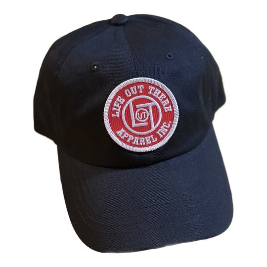 A black LOT Snapback "Dad Hat" Trucker Hat from Life Out There Apparel, featuring a red and white embroidered patch on the front. This adjustable cap displays a circle with the text "Life Out There Apparel Inc." and a stylized illustration of a tent.