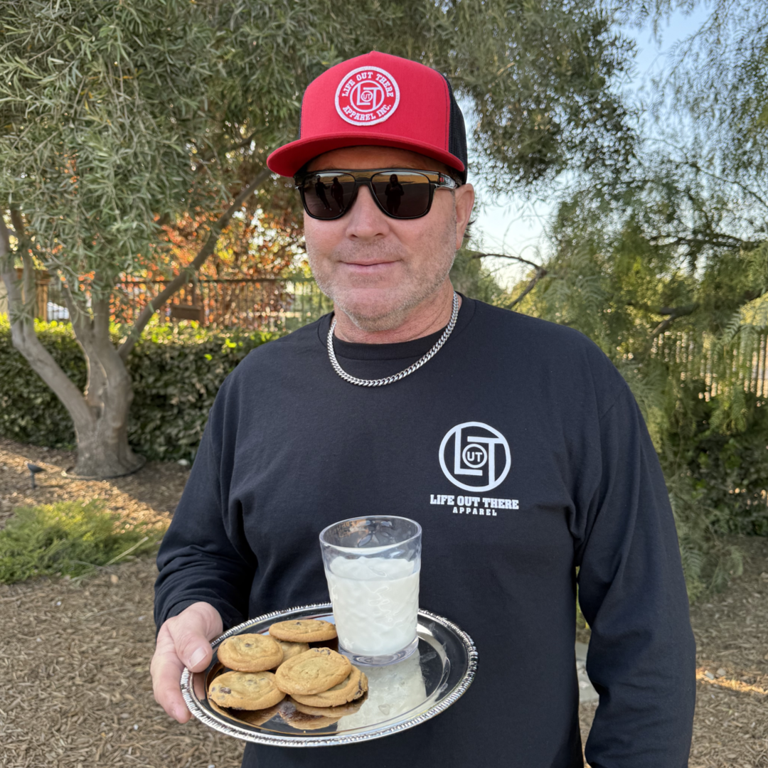 Black shirt with a cartoon cookie wearing a Santa hat and sunglasses labeled "2024," alongside glass milk cartons. Text reads, "Life Out The Apparel.