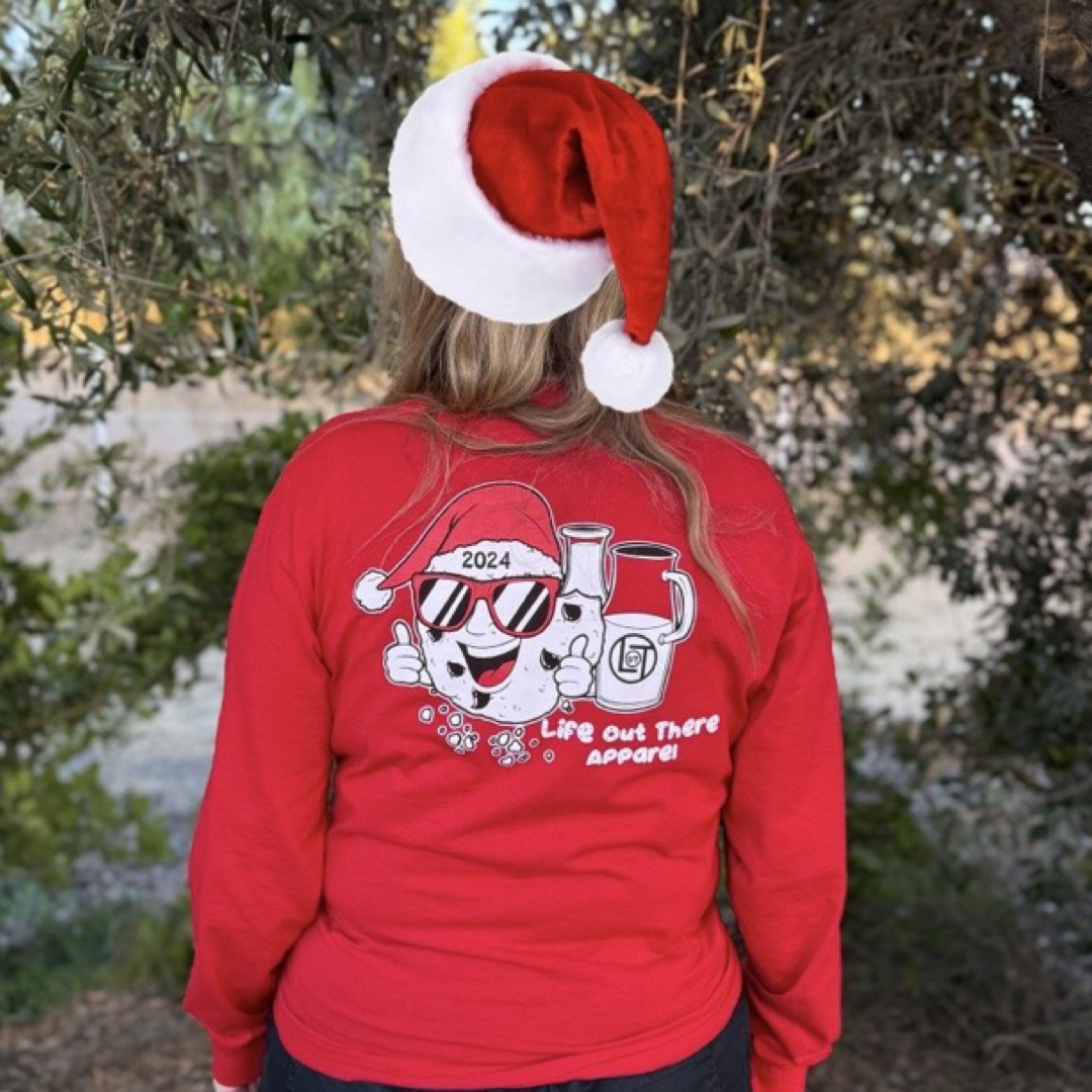 Red shirt with a cartoon cookie wearing a Santa hat and sunglasses labeled "2024," alongside glass milk cartons. Text reads, "Life Out The Apparel.