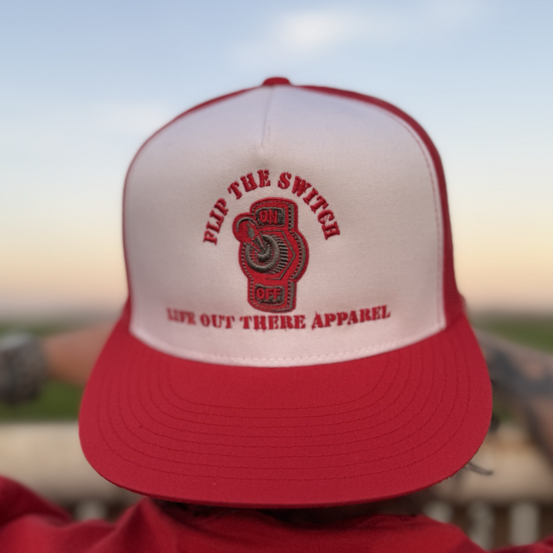 The FLIP THE SWITCH - Flat Bill SnapBack Trucker Hat in Red/White by Life Out There Apparel features a switch graphic and the text FLIP THE SWITCH. With a blurred sunset background, its ideal for celebrating your favorite adventure brands anniversary launch.
