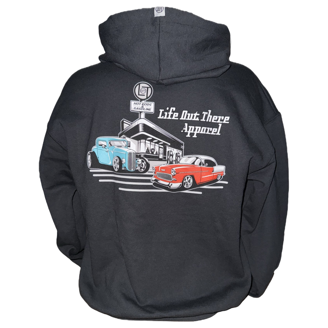 The Unisex Cruzin Zip-Up Hoodie in black by Life Out There Apparel features a blue and red Chevy Bel Air at a retro gas station graphic, plus logo on the back—an ideal Father’s Day gift.