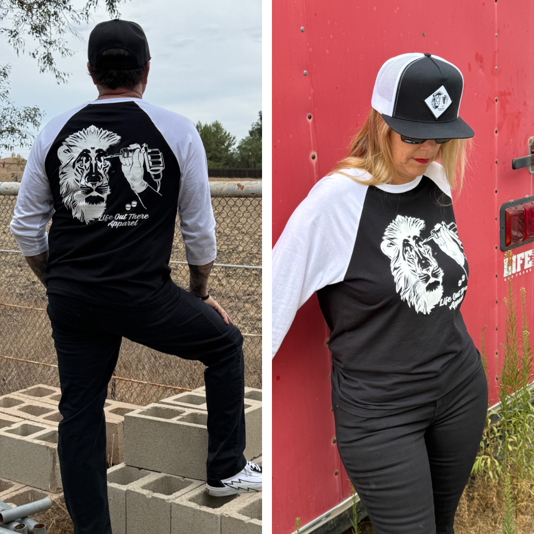 Two people wear matching Life Out There Apparel Unisex - Not All There 3/4 Sleeve Raglan T Shirts in black and white. Each tagless shirt features a lion and fist graphic with text on the back, plus a lion design on the front. They pose by a fence and red wall outdoors.