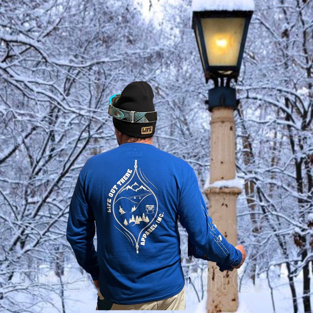 The Royal Blue Life Out There Apparel “Snow B. U. M. P. “ Unisex long sleeve tee has a snowboard mountian scene design coming out of an unzipped zipper on the back of the shirt & a chair lift going down the right sleeve. Here is a man and a woman showing the back of the shirt while holding snowboards.