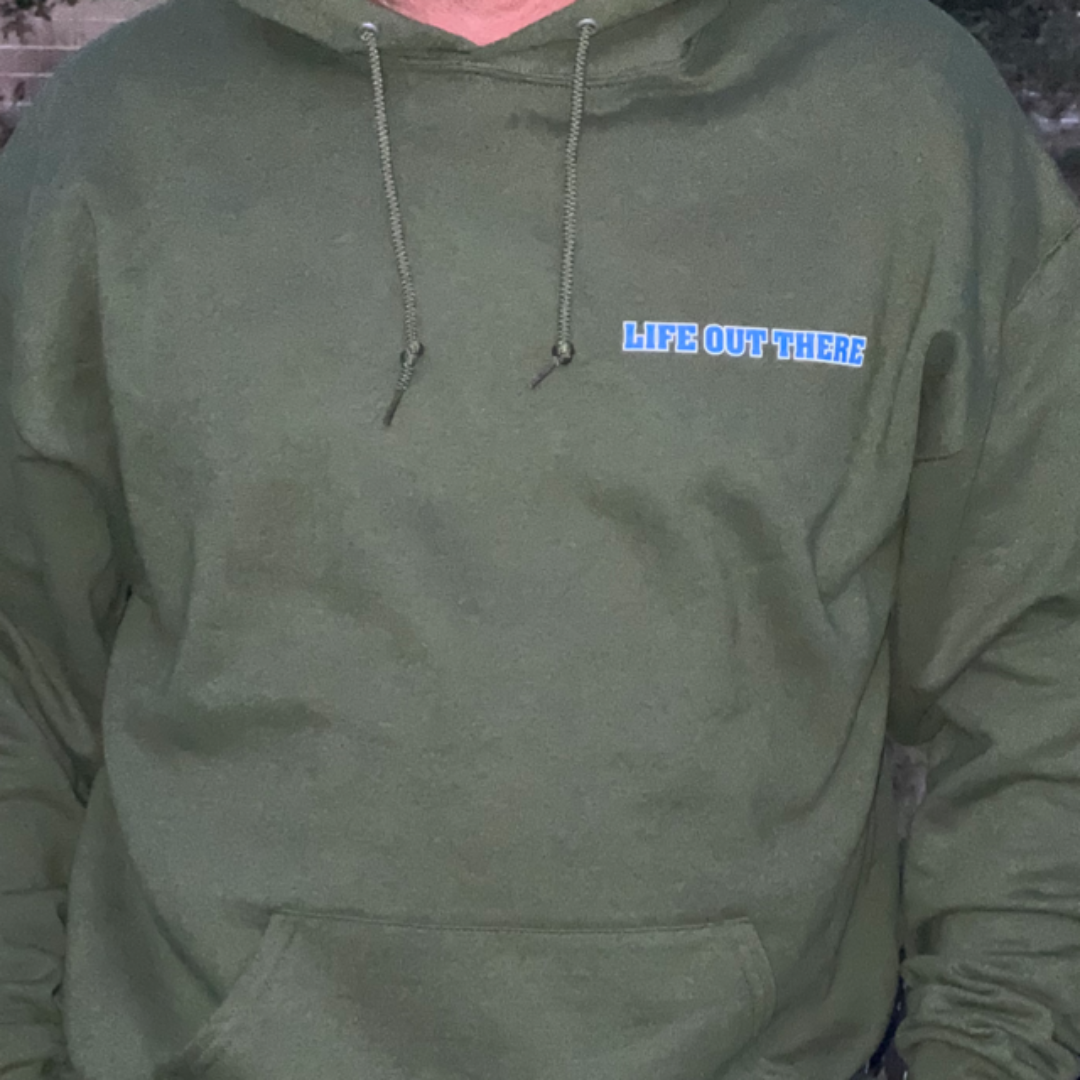 A person wearing the Unisex The Freedom Hoodie in Military Green by Life Out There Apparel, featuring a small logo that reads LIFE OUT THERE on the upper chest, captures the essence of American values with its design.