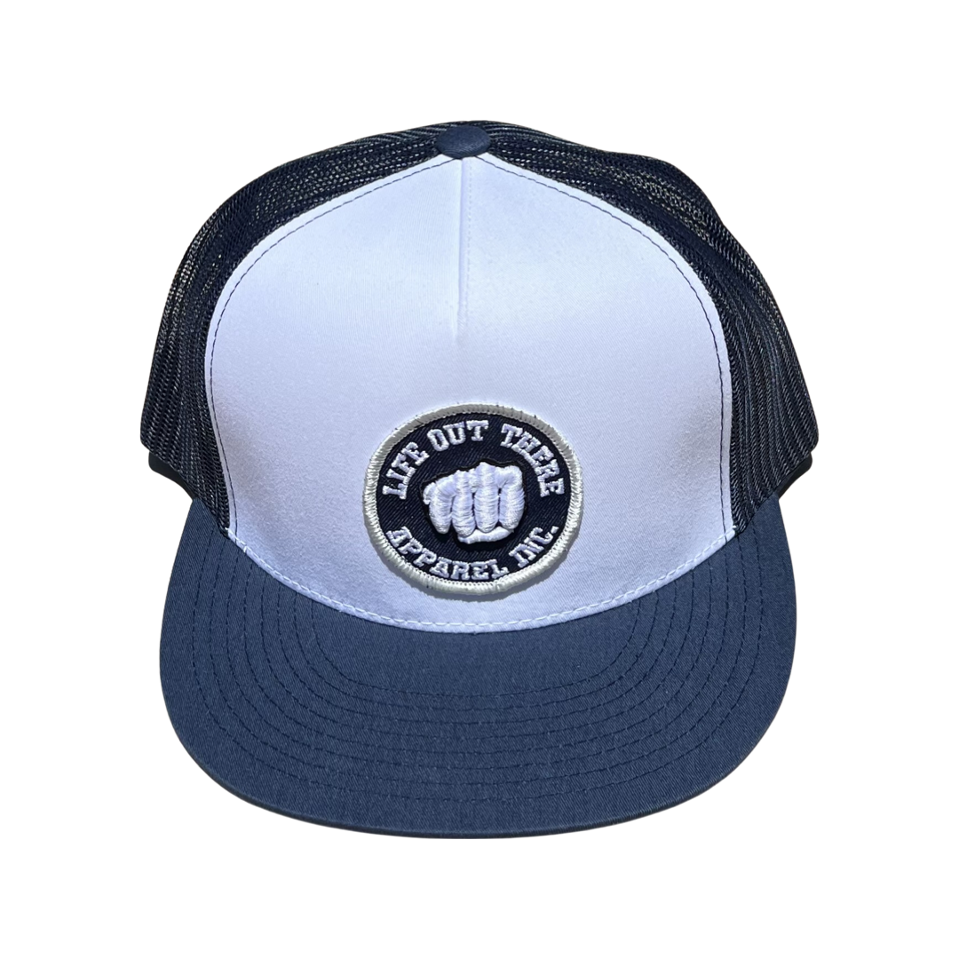 The Pound It - 3D Puff Embroidered Snapback Trucker in navy and white by Life Out There Apparel features a distinctive circular patch with a clenched fist design and the words "LIFE OUT THERE APPAREL INC." in black and white. This stylish Snapback adds an edgy touch to any outfit.