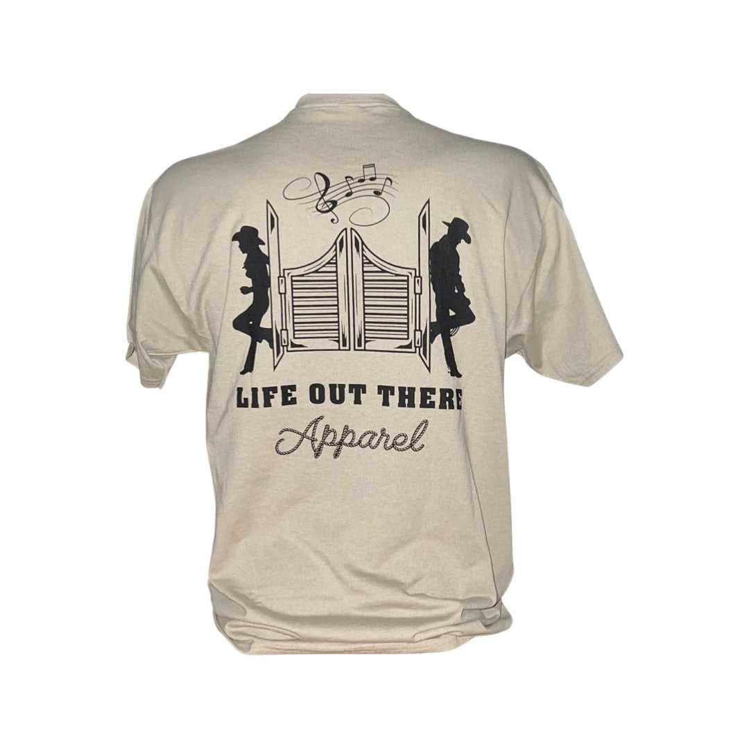 This sandstone and black unisex T-shirt in XXL from Life Out There Apparel features a design of two silhouettes sitting back-to-back by saloon doors with musical notes above, making it an ideal choice for cowboy enthusiasts and country music lovers.