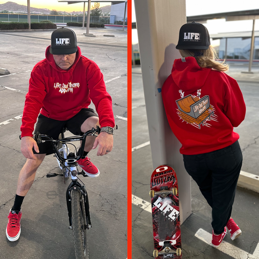 Life Out There Apparel “Fun is Not a Crime” Red Unisex hoodie has a skateboarder and bmx rider having fun on a half pipe skateboard ramp. A man wearing the hoodie sitting on a bmx bike and a woman showing the back of the hoodie holding a skateboard. 