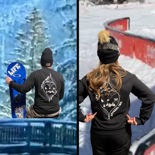The Black Life Out There Apparel “Snow B. U. M. P. “Unisex  long sleeve tee has a snowboard mountian scene design coming out of an unzipped zipper on the back of the shirt & a chair lift going down the right sleeve. This photo has a man sitting on a railing with a snowboard & - lady standing next to a snowboarding hand rail. 