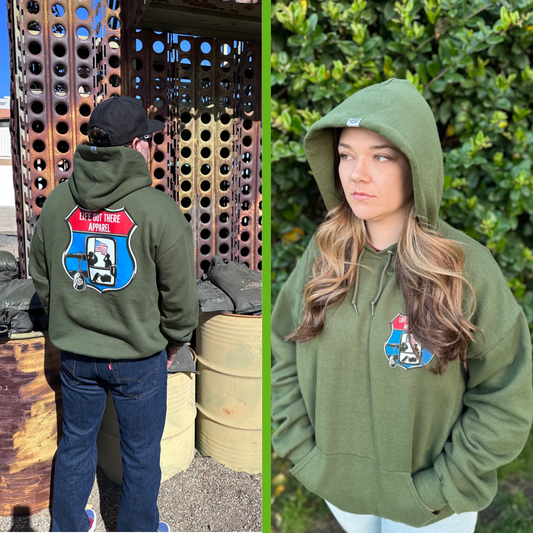 Military Green Unisex Pullover hoodie from Life Out There Apparel “Leave It Behind” the design has a truck side mirror with the reflection of a male, female & K9 soldiers saluting the American flag - bringing awareness to P. T. S. D. (post traumatic stress disorder). This is a photo,of a man wearing the hoodie showing the back design, standing next to a bunker & a women showing the front design. 