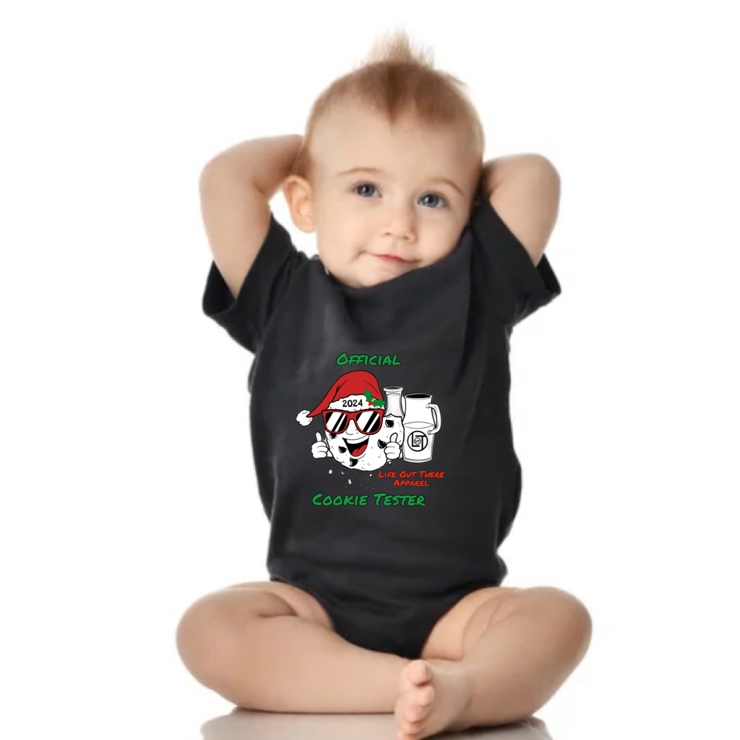 Black short sleeve baby shirt with a cartoon cookie wearing a Santa hat and sunglasses labeled "2024," alongside glass milk cartons. Text reads, "Life Out The Apparel / official cookie tester”. 