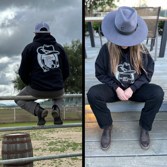 Life Out There Apparel “ONWARD & UPWARD” Tour Black Unisex hoodie is a country concert design with a cowboy hat & horseshoe on the front and back with every Life Out There Apparel launch for the past 2 years. This photo shows a man sitting on a ranch gate & a woman wearing a cowboy hat sitting on a deck.   