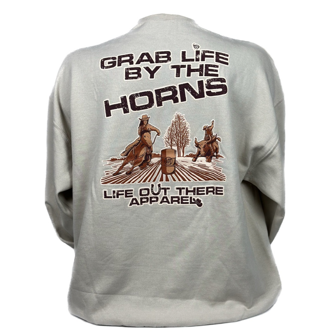 Life Out There Apparel Sandstone colored “Grab Life By The Horns” Unisex Crew Neck Sweatshirt has a girl barrel racer getting ready to turn around a barrel with a guy riding a bull behind her.  This shows the back of the sweatshirt. 