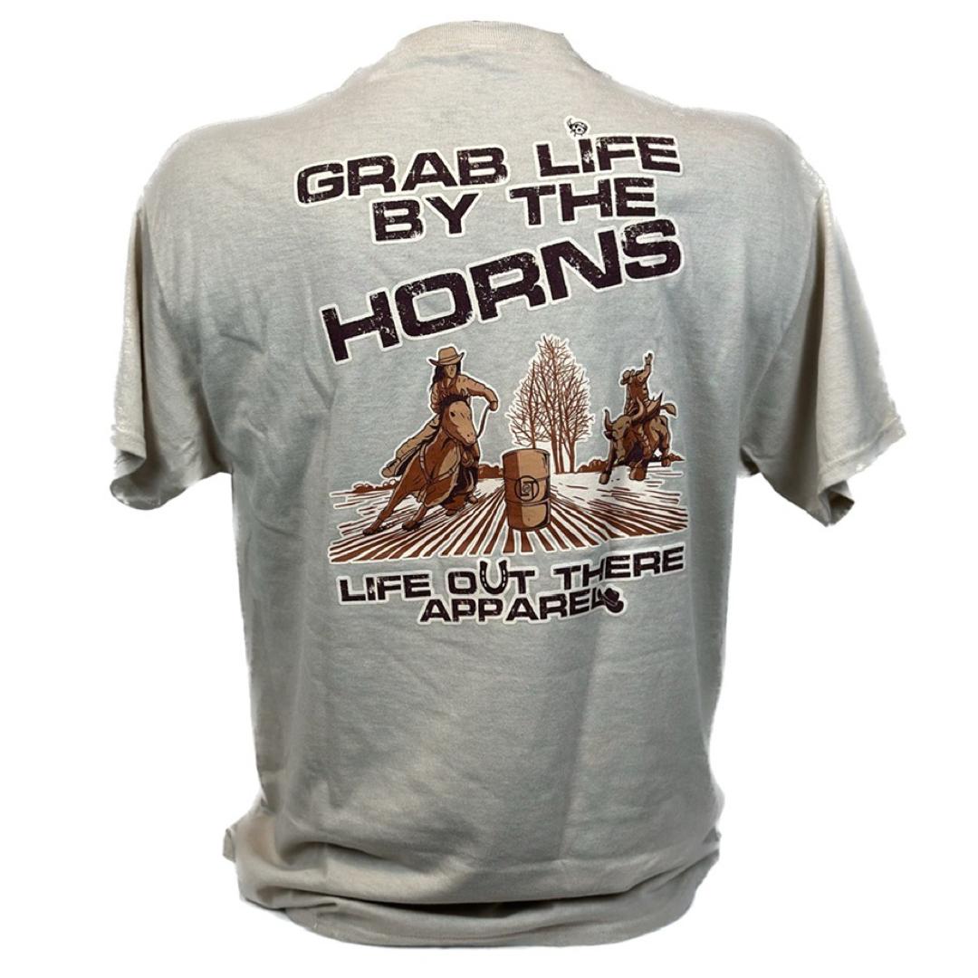 Life Out There Apparel Sandstone colored “Grab Life By The Horns” Unisex tee shirt has a girl barrel racer getting ready to turn around a barrel with a guy riding a bull behind her.  This shows the back of the tee shirt on a transparent background. 