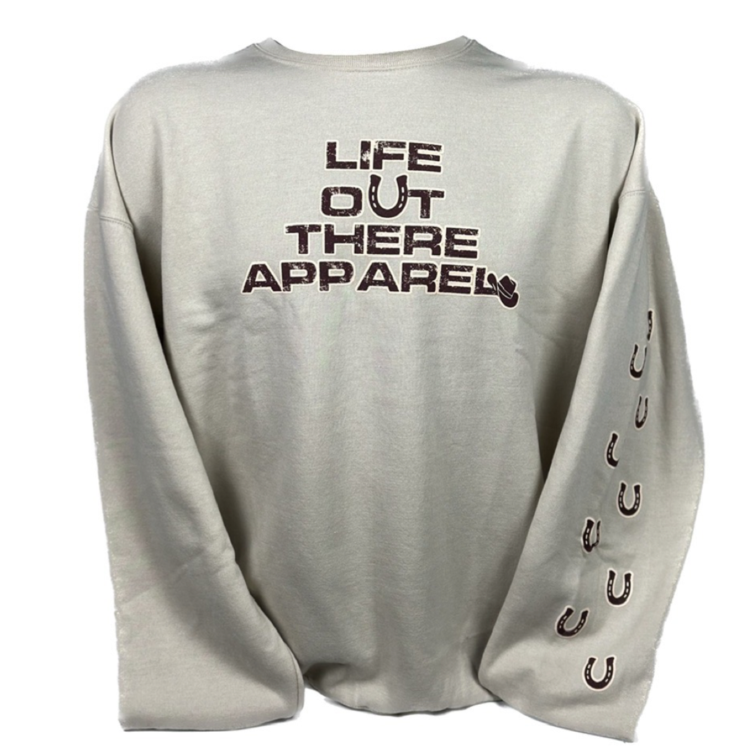 Life Out There Apparel Sandstone colored “Grab Life By The Horns” Unisex Crew Neck Sweatshirt has a girl barrel racer getting ready to turn around a barrel with a guy riding a bull behind her.  This shows the front of the sweatshirt. 