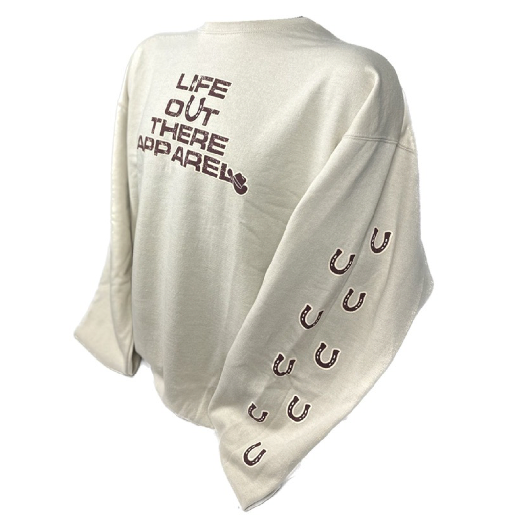 Life Out There Apparel Sandstone colored “Grab Life By The Horns” Unisex Crew Neck Sweatshirt has a girl barrel racer getting ready to turn around a barrel with a guy riding a bull behind her.  This shows the front of the sweatshirt & the sleeve which has horseshoes up the sleeve. 