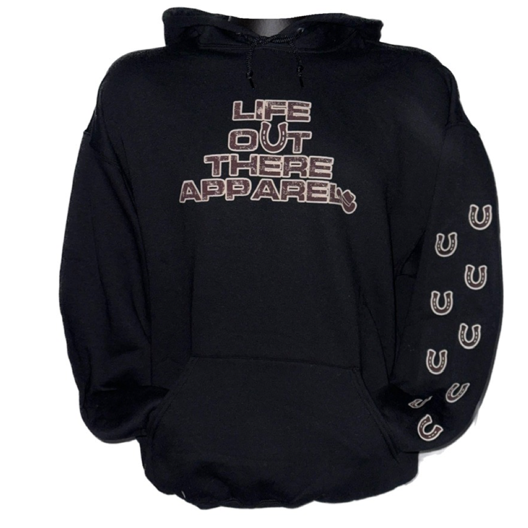 Life Out There Apparel “Grab Life By The Horns” Black Unisex Hoodie has a girl barrel racer getting ready to turn around a barrel with a guy riding a bull behind her.  This shows the front & sleeve of the black hoodie with a transparent background. 