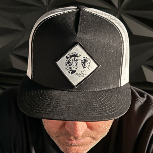 A person wears the Not All There - Flat Bill SnapBack Trucker Hat in Black/White by Life Out There Apparel, featuring a diamond lion-and-lamb patch and NOT ALL THERE subtly embroidered on the brim, partially obscuring their face.