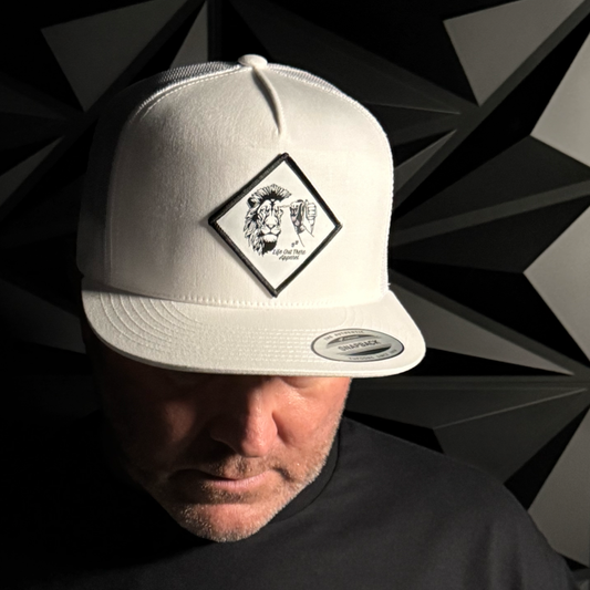 A man in a black shirt wears the Not All There - Flat Bill SnapBack Trucker Hat in white by Life Out There Apparel. The hat features a diamond patch with a lion, hand graphic, and NOT ALL THERE. Angular patterns fill the dark background.