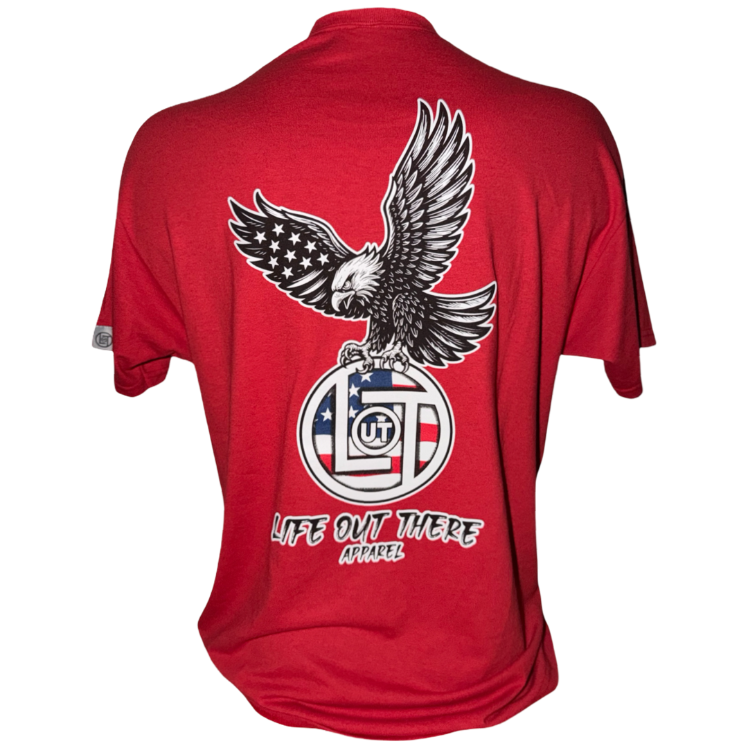 The Flight of Freedom Tee - Red by Life Out There Apparel is a tagless, comfortable cotton-polyester unisex shirt featuring a graphic of a bald eagle landing on a U.S. flag emblem and "LIFE OUT THERE APPAREL" in white text below.