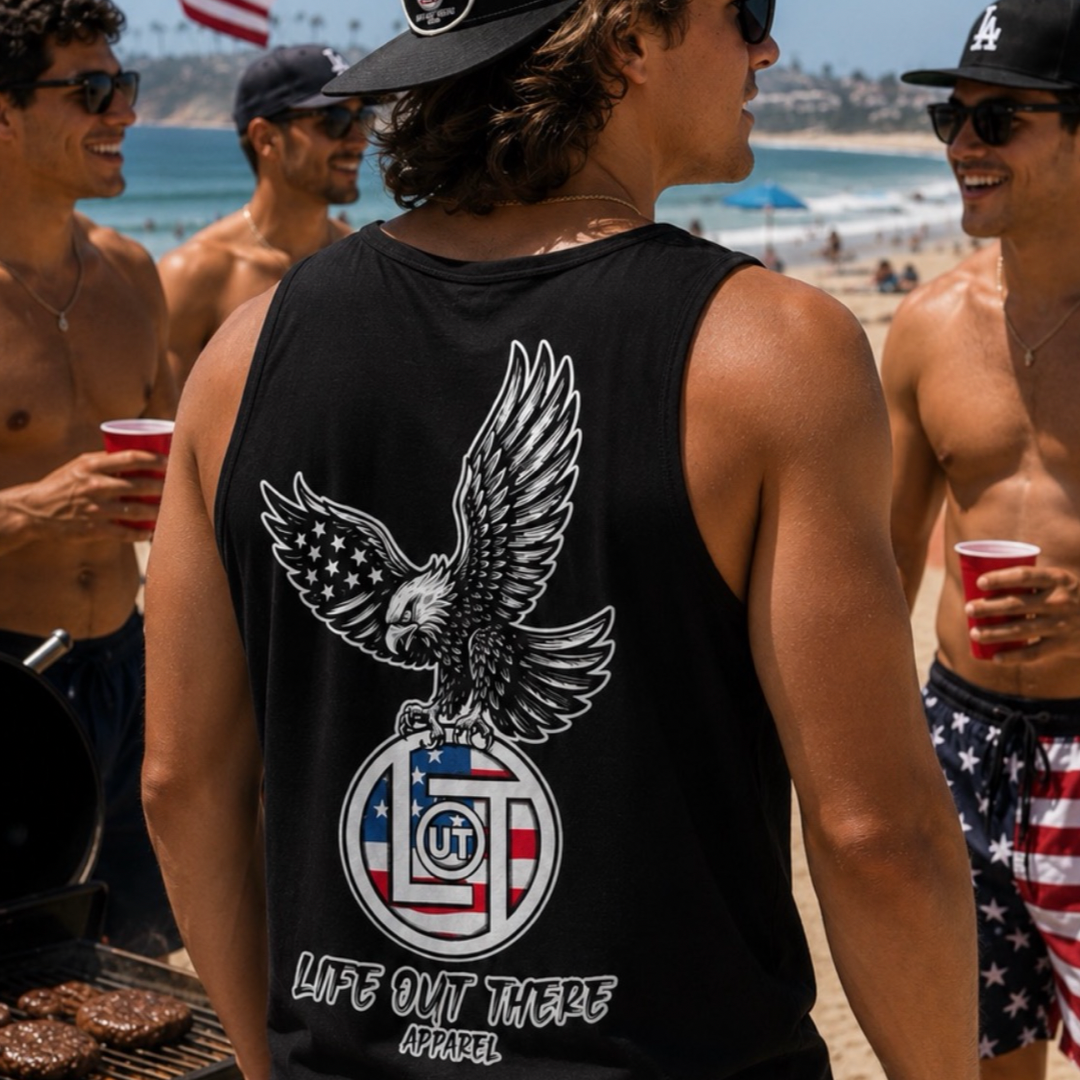 A group of men enjoy a sunny beach day. One stands out in the Life Out There Apparel Flight of Freedom Tank Top - Black, featuring an eagle and American flag design. Others hold red cups and smile.