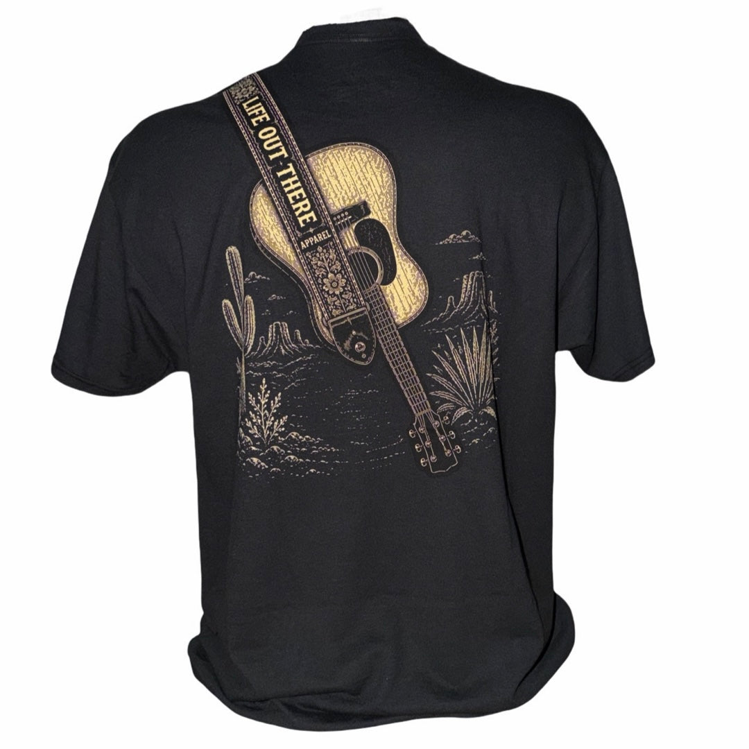 The Category Hurricane Tee - Black by Life Out There Apparel is a unisex T-shirt made from a soft cotton polyester blend, showcasing a back graphic of an acoustic guitar, cacti, and desert scenery. The tagless design offers extra comfort, and the guitar strap boldly displays the message SEE YOU OUT THERE.