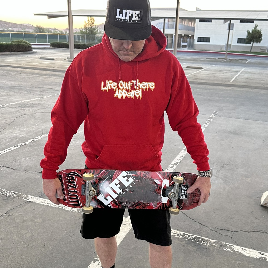 Life Out There Apparel “Fun is Not a Crime” Red Unisex hoodie has a skateboarder and bmx rider having fun on a half pipe skateboard ramp. A man showing the front of the hoodie, holding a skateboard. The front design looks like it’s spray painted. 